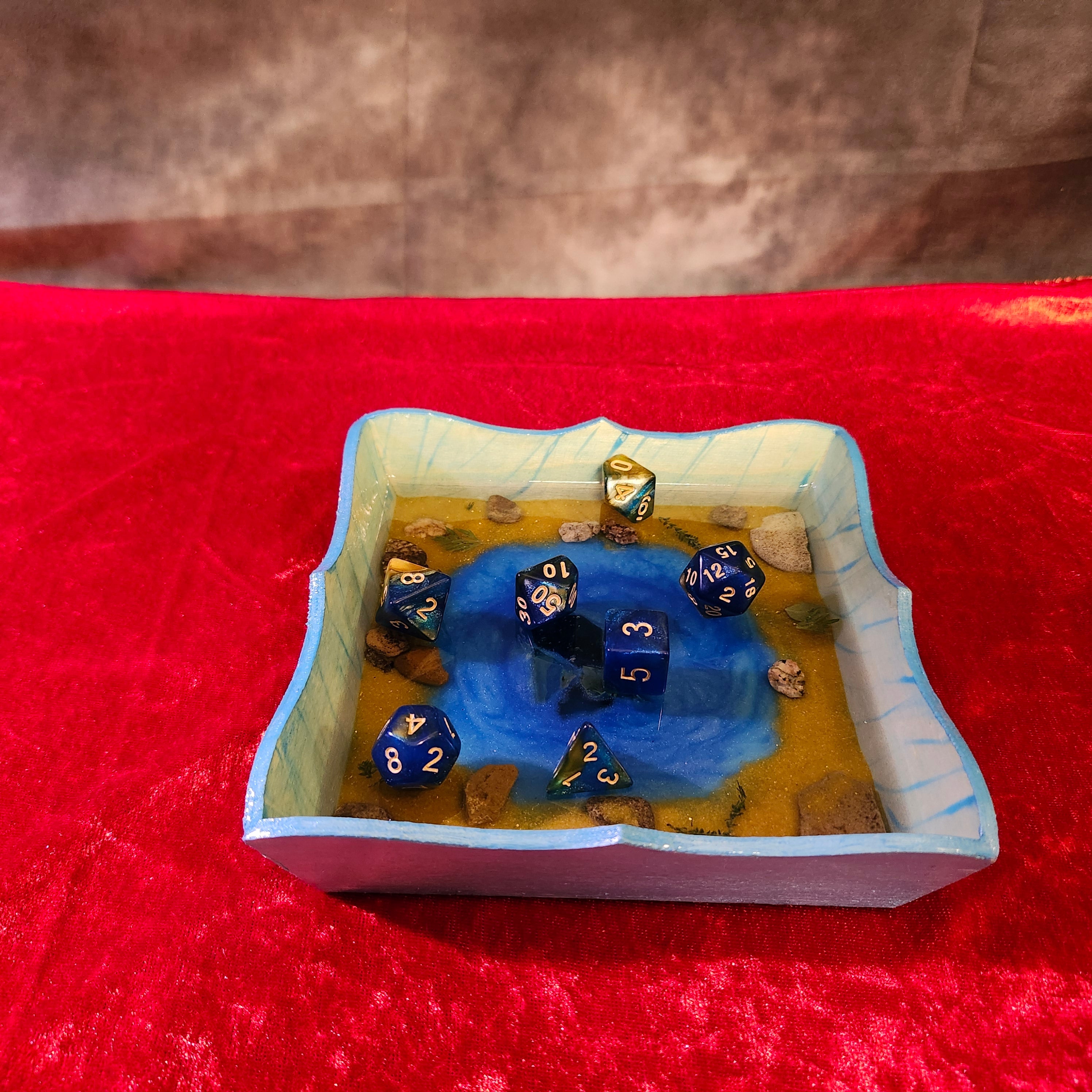 Handcrafted Azure Oasis resin dice tray featuring a multi-toned blue gradient fluid art pool, a central dark crystal cluster, and natural stone terrain shorelines.