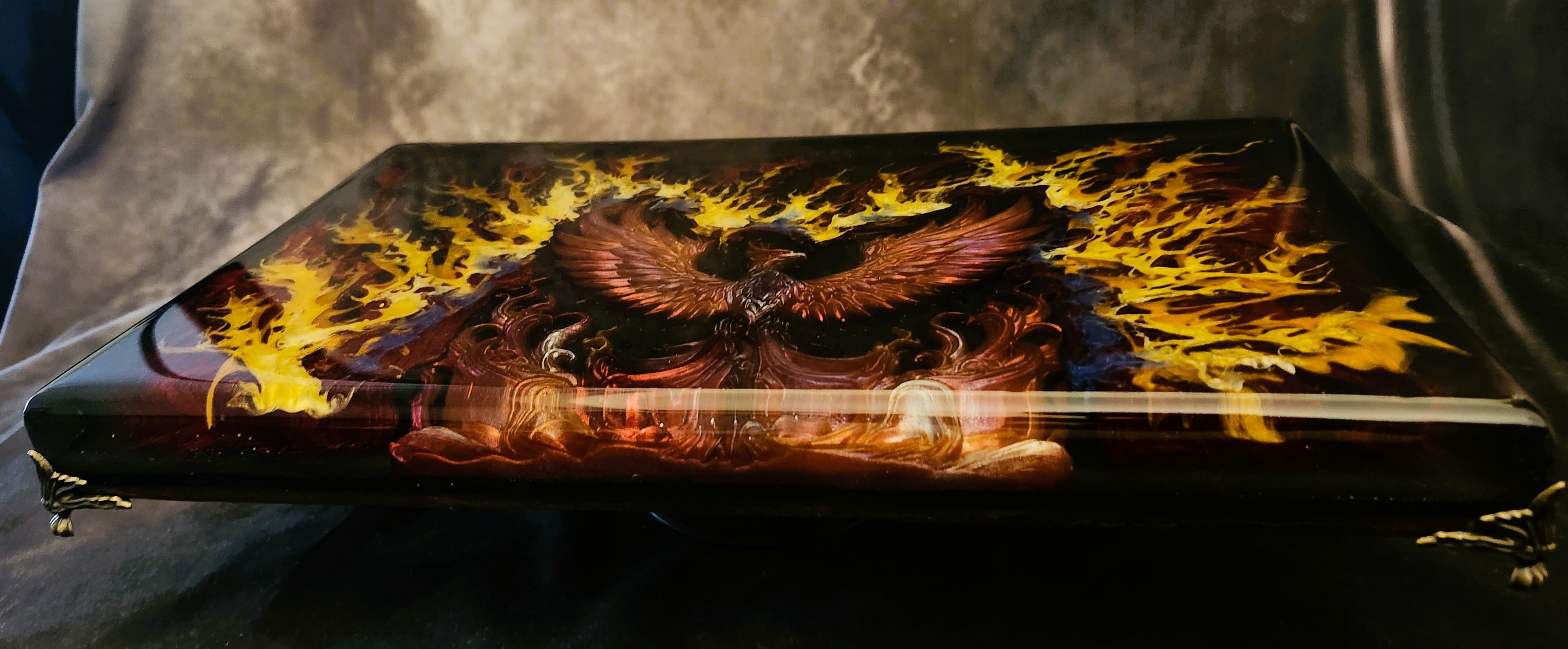 3D sculpted phoenix resin display riser tray with vibrant yellow and orange flame fluid art, elevated on four premium polished gold corner legs.